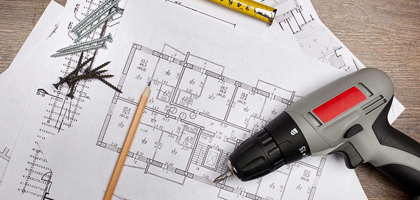 Building plans partly covered with a tape measure, pencil, drill and screws